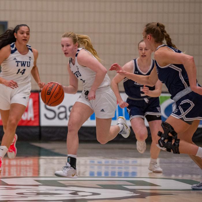 Girls in white and blue jerseys playing basketball.