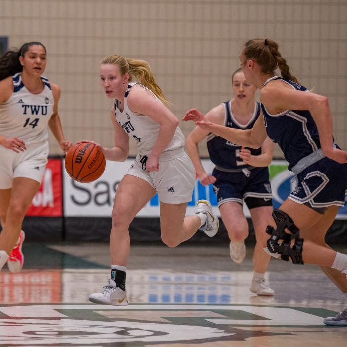 Girls in white and blue jerseys playing basketball.
