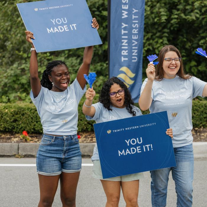 Three TWU students holding welcome signs during orientation day on the Langley campus.