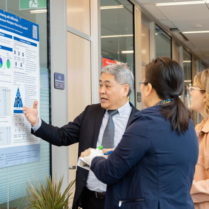 A presenter discusses a research poster with two attendees during a poster presentation.