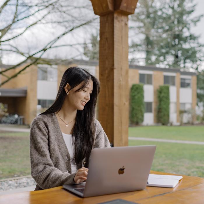 Student working on a laptop at an outdoor table on the TWU campus.