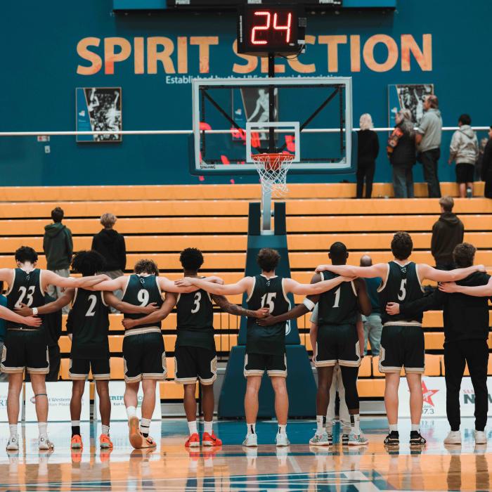 Basketball players stand together on a gymnasium court before a game.