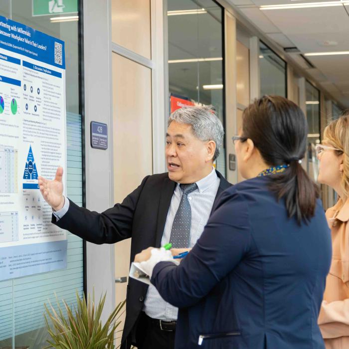 A presenter discusses a research poster with two attendees during a poster presentation.