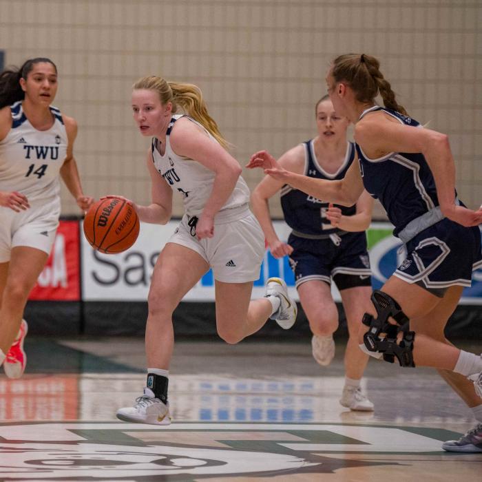 Girls in white and blue jerseys playing basketball.